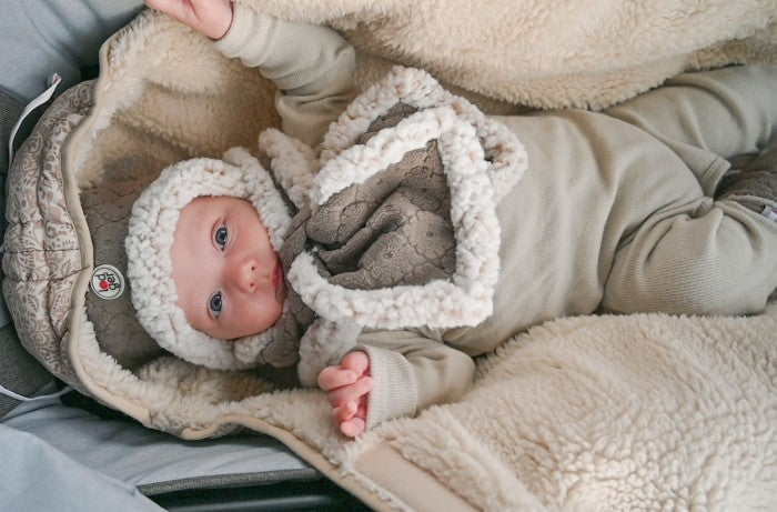 Lodger Hatter Folklore Fleece cepure buffalo krāsa, bildē bērns guļammaisā ar cepuri un šalli.