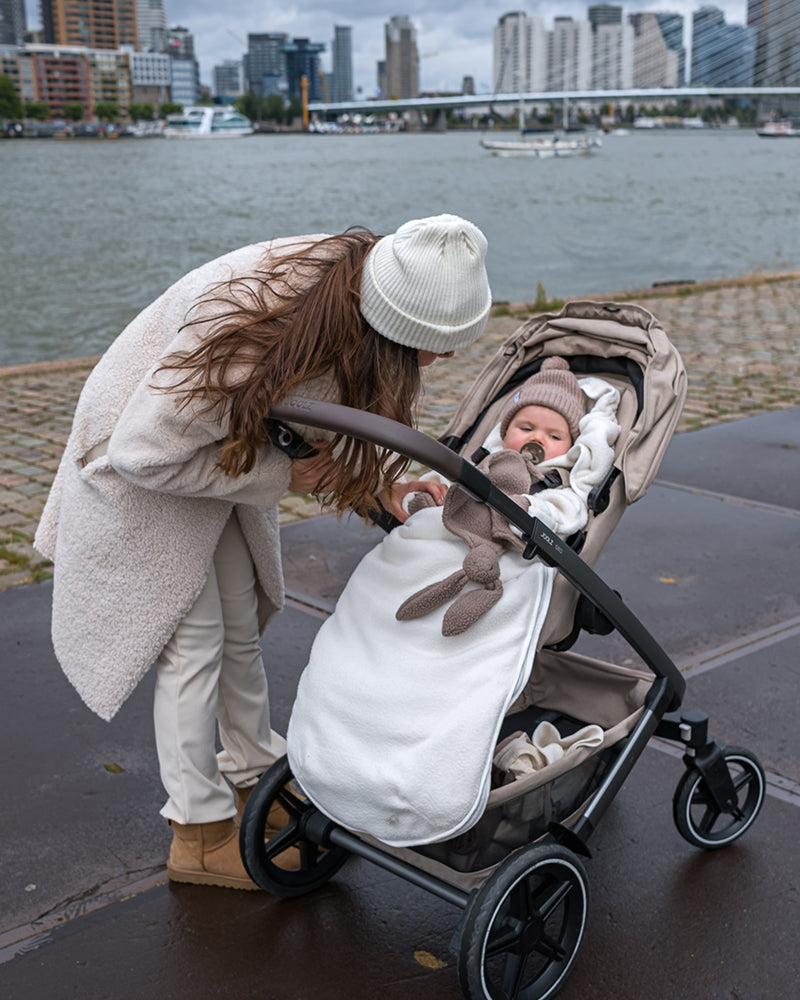 Lodger Mini Bunker Teddy vissezonas guļammaiss cloud dancer krāsa, bildē mazulis ir ratiņos ar guļammaisu.