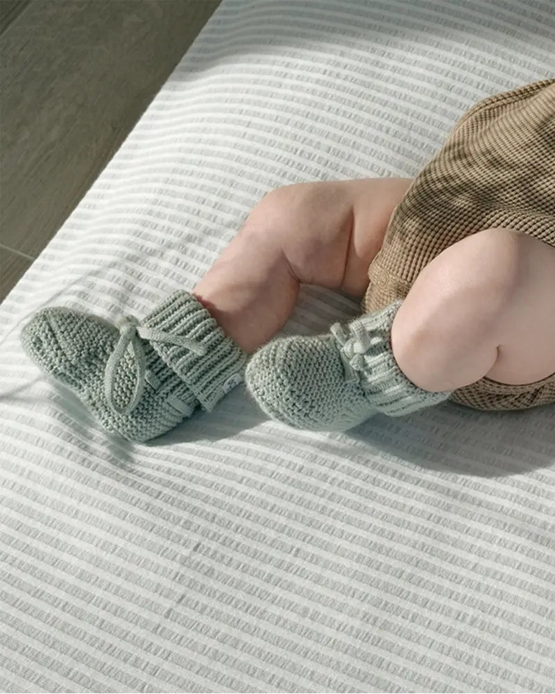 Lodger Slipper knit kokvilnas čībiņas silk krāsā. Redzamas no sāna uzvilktas mazuļa kājiņās.