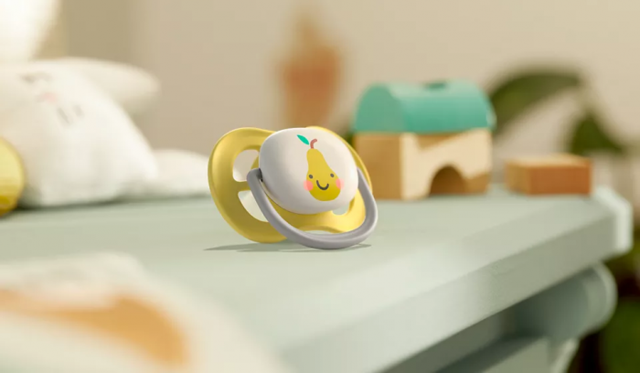 Philips Avent Māneklītis Ultra Air Deco, redzams dzeltens māneklītis ar ābola zīmējumu, novietots uz galda.
